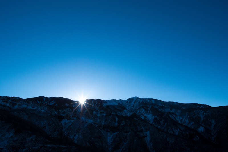 bright sun emerging from behind a snowy mountain ridge during sunrise, sunrise over mountains in hakusan 4k
