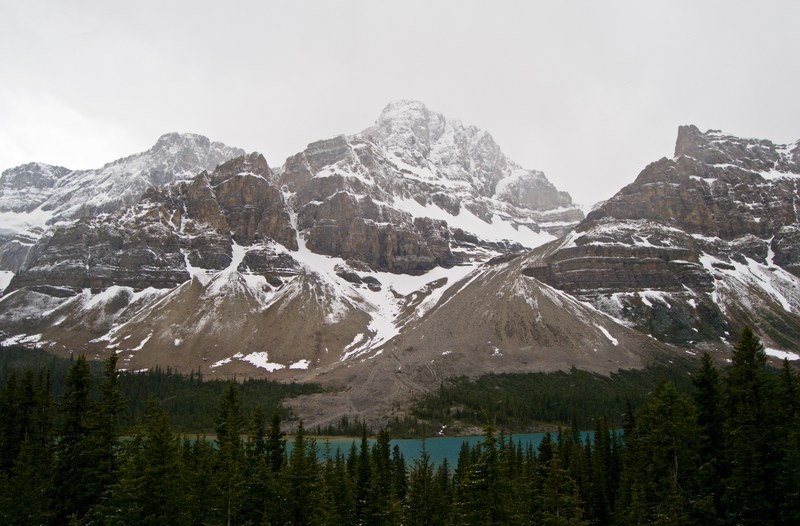 on a cloudy winter day in canada snow covers a rocky mountain range flanked with pine trees surrounding a lake, canadas snowy rocky mountains 4k