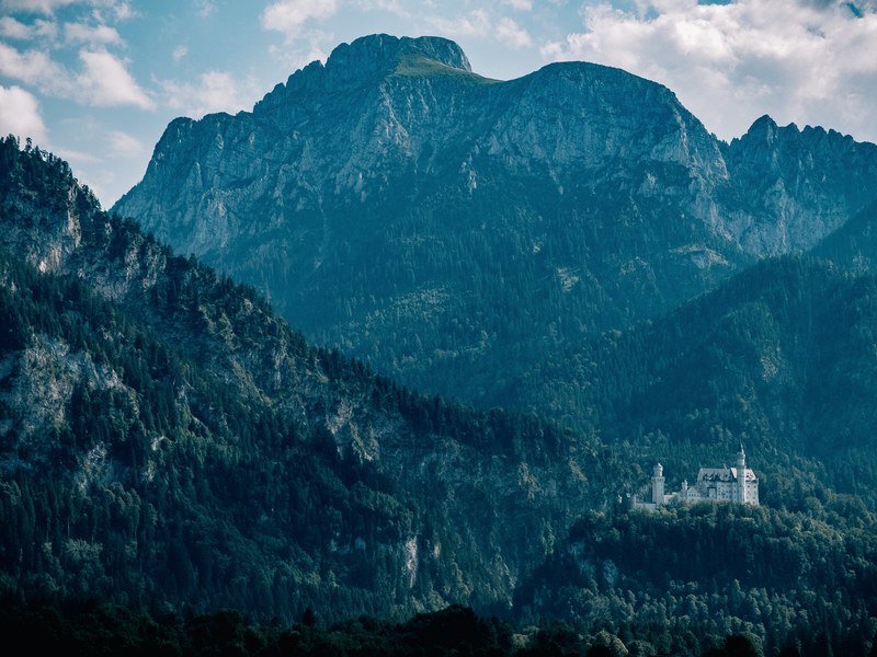a scenic landscape with a rugged mountain ridge towering over the neuschwanstein castle, mountains by neuschwanstein castle 4k