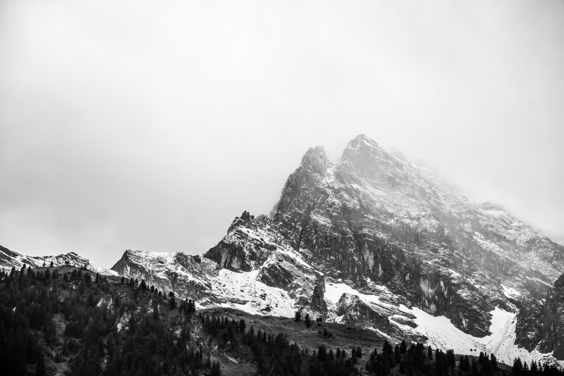 a jagged snow capped mountain against a pale white sky, silver mountain in fog 4k