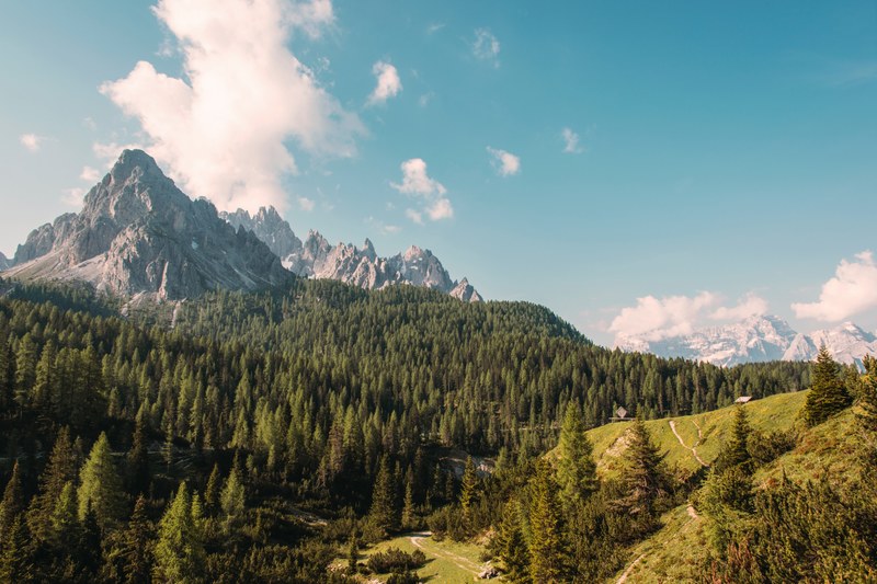 jagged mountains towering over wooded hills on a bright day, rugged mountains and blue sky 4k