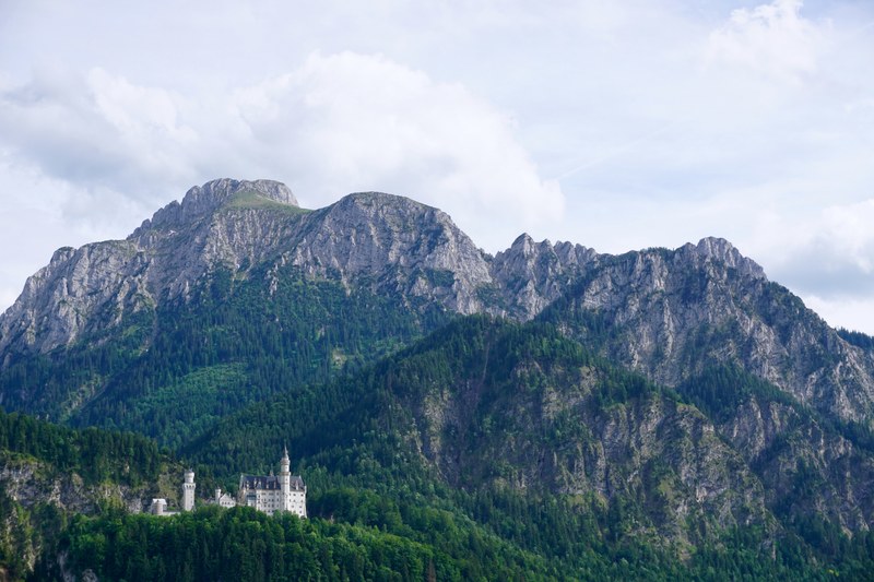 distant view of the neuschwanstein castle on a wooded mountain slope, neuschwanstein on a warm day 4k