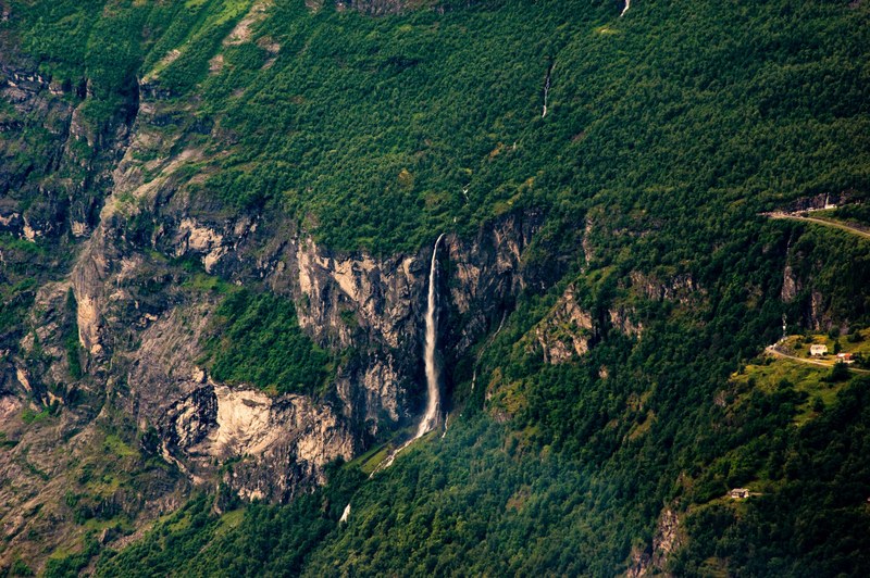 a drone shot of a waterfall tumbling from a rocky face into a green forest, remote waterfall from above 4k