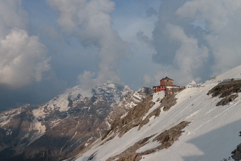 a building touches the clouds on top of a snow covered rocky mountain, building on a snowy mountain 4k