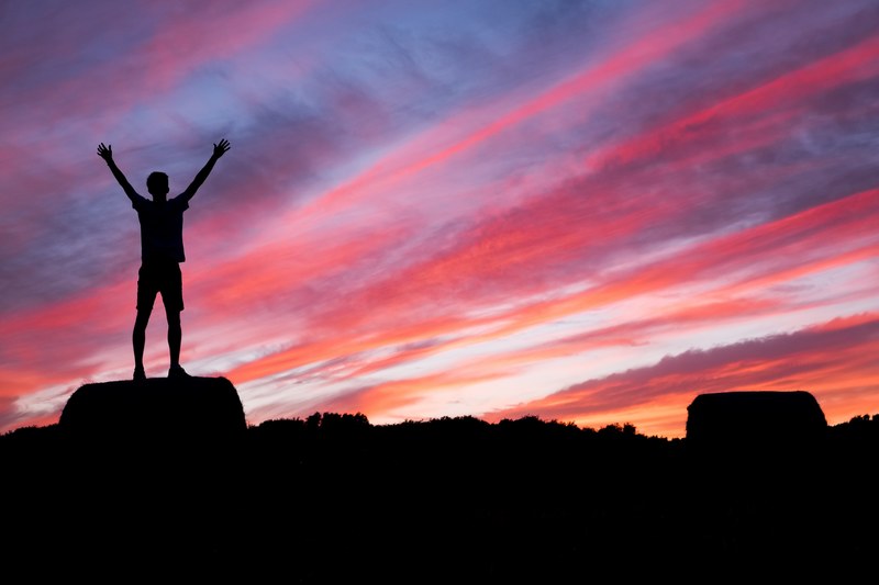 a silhouette of a man lifting up his hands while while standing on a rock at sunrise, reach out to the world 4k