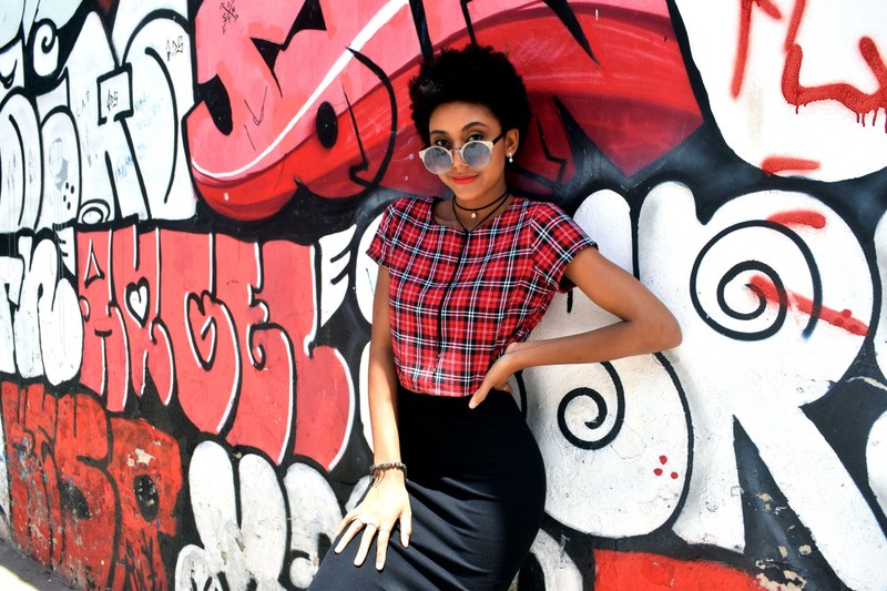 a woman in a plaid shirt leans against a black red and white graffitied wall, power 4k