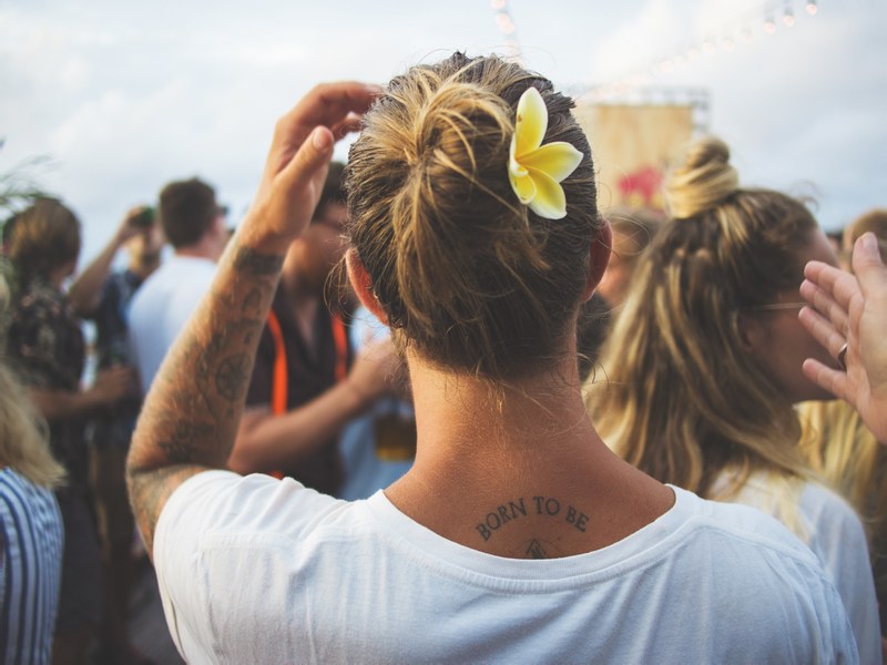 a person with tattoos and a flower in their hair looks toward a festival crowd, looking into festival crowd 4k