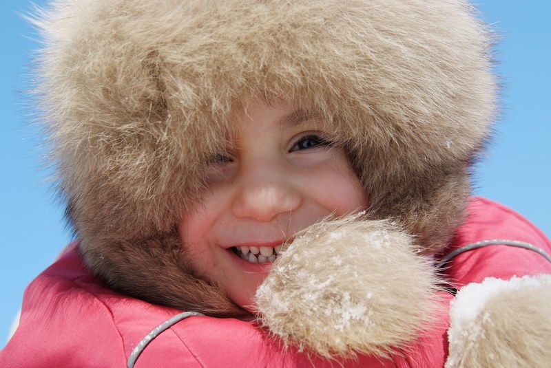 a child wearing a fur lined hood smiles against a blue sky in kazan, winter playground smile 4k