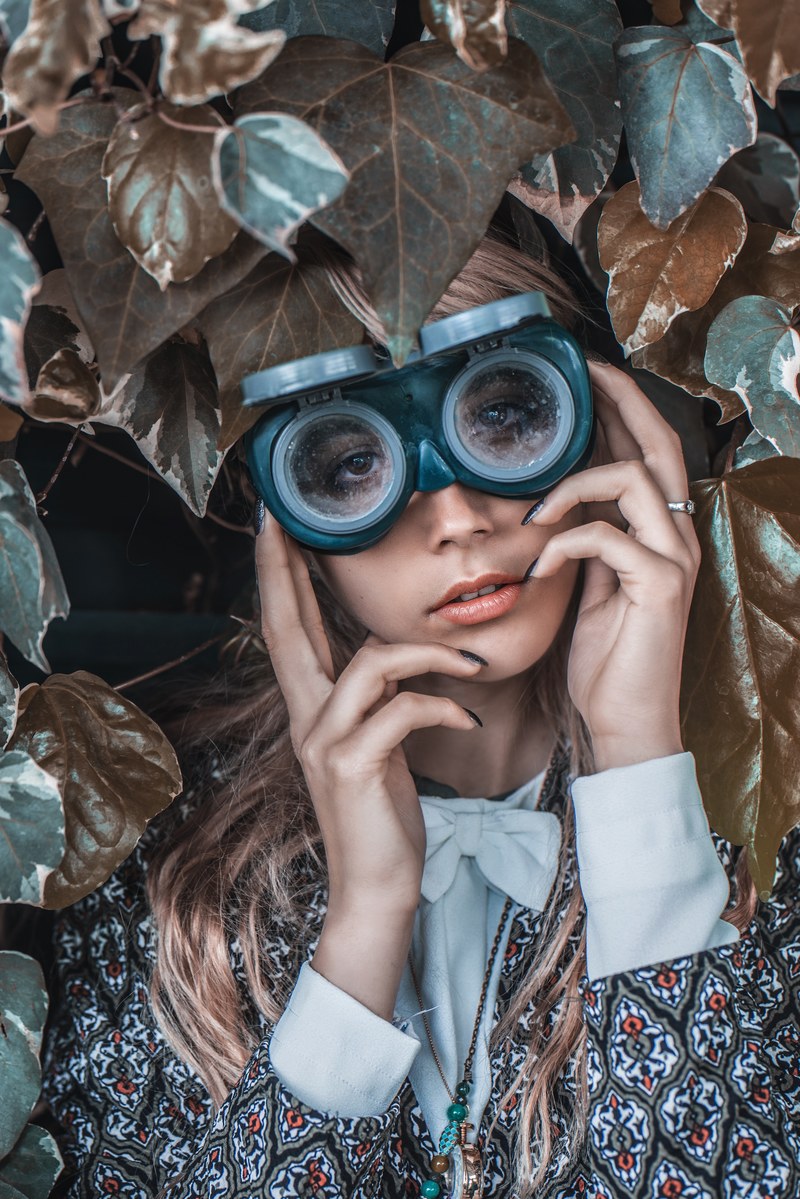 woman models steampunk goggles while shrouded in brown leaves, fixation 4k