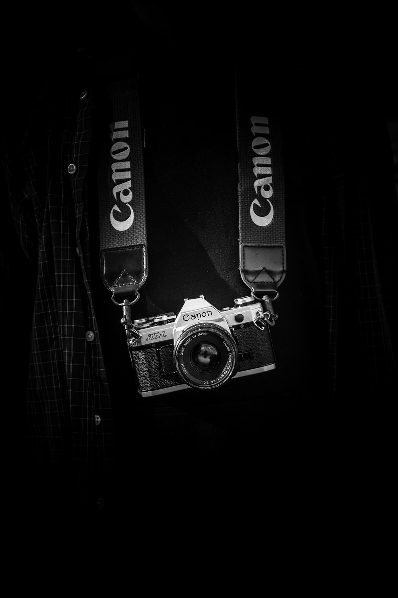 black and white shot of canon camera with strap on torso with checked shirt, monochrome canon camera hangs 4k