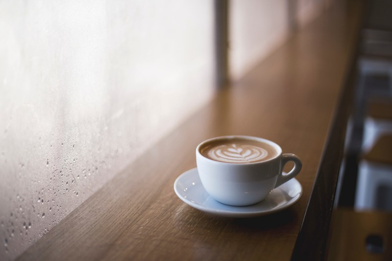 a cup of coffee in a white mug with a leaf in the froth on a bar in nashville, crema nashville 4k