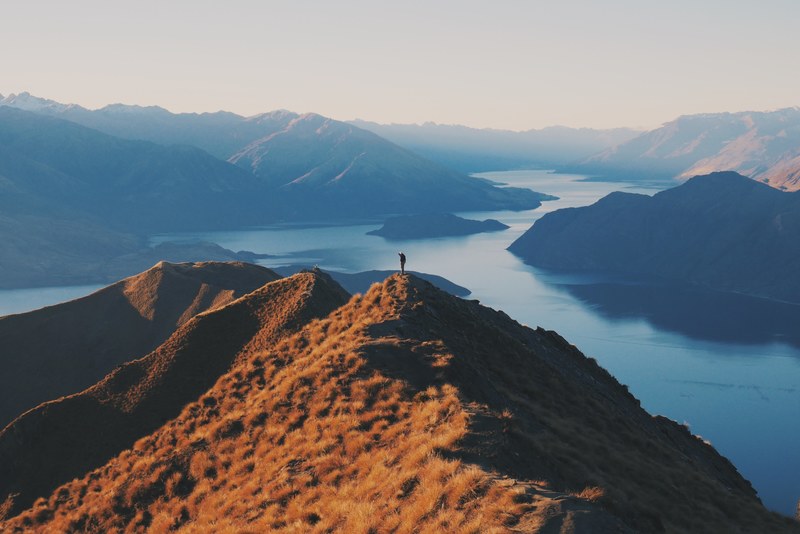 a silhouette of a person on a grassy mountain peak over a lake, mountain peak solitude 4k
