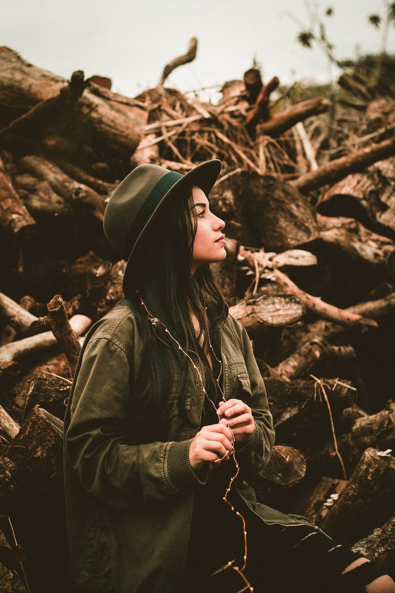 young woman with a hopeful expression wearing christmas lights in a pile of logs, by the wood pile 4k
