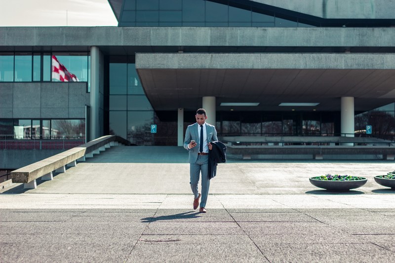 a man in a formal suit checking his smartphone while walking out of an office building, businessman leaving the office 4k