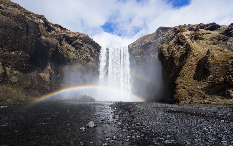 a magnificent shot of a waterfall tumbling down from a rock with a small rainbow in the spraying water, rainbow under skgafoss waterfall 4k