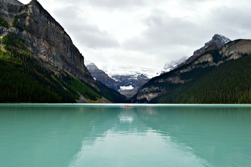 a red boat on the turquoise surface of lake louise surrounded by jagged mountains, boat on lake louise 4k