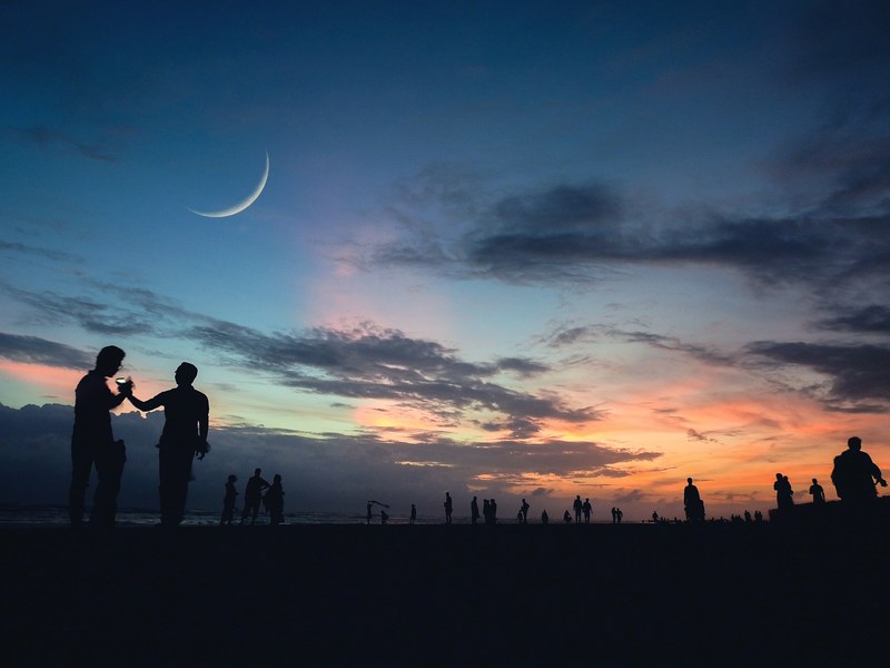 people silhouetted against a twilit sky pinned with a crescent moon at coxs bazar, first moon 4k