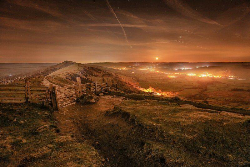 a wooden gate with fences on a mam tor hilltop overlooking the glowing fires and lights in the village, afterglow 4k
