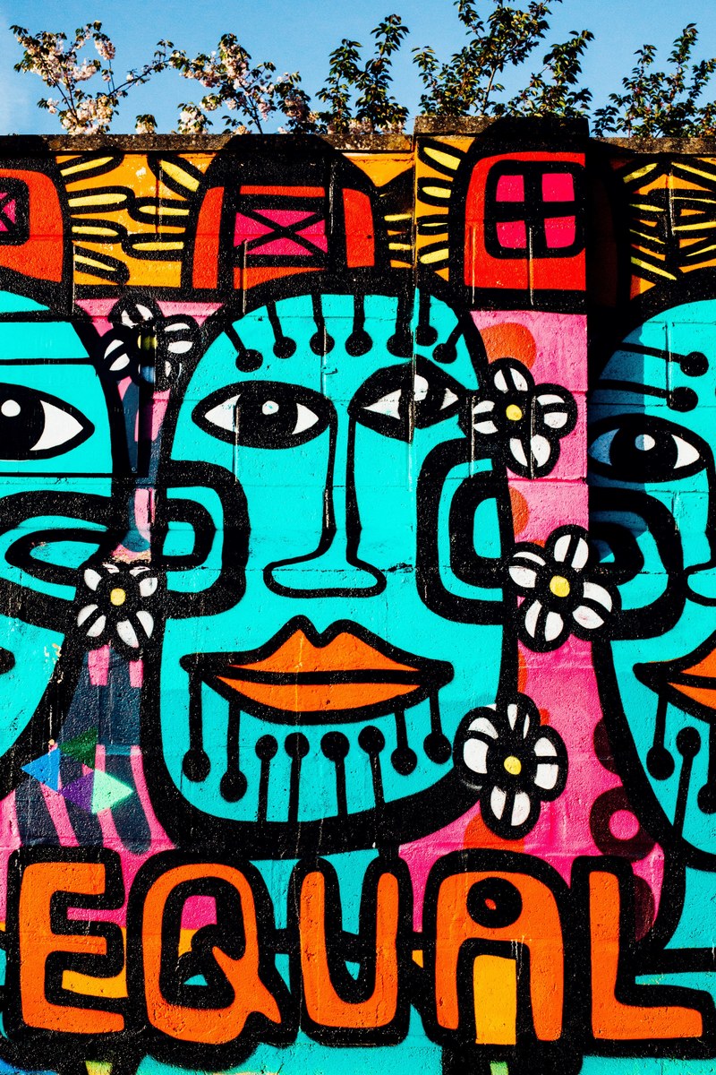 brightly colored urban graffiti mural artwork on wall with equal text and tribal faces, brick wall painting of faces 4k