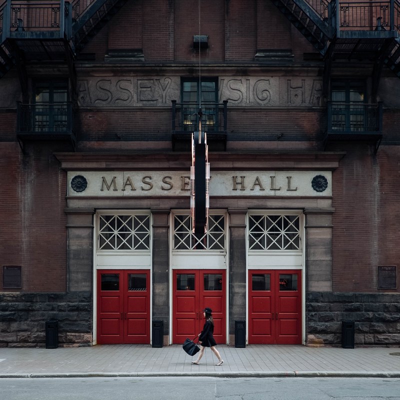 a woman in a black dress passing by massey hall in toronto, massey hall entrance 4k