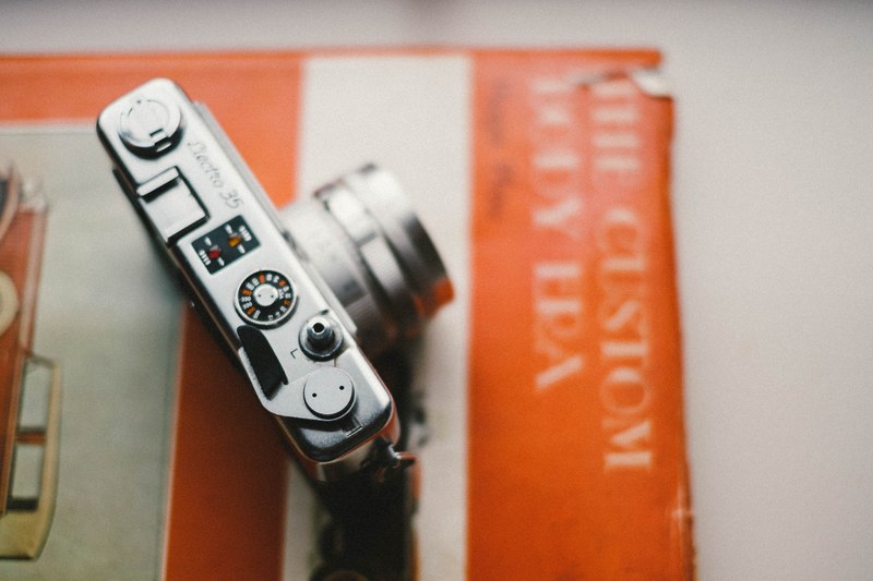 looking down on a camera that sits atop an orange vintage book, camera on old orange book 4k