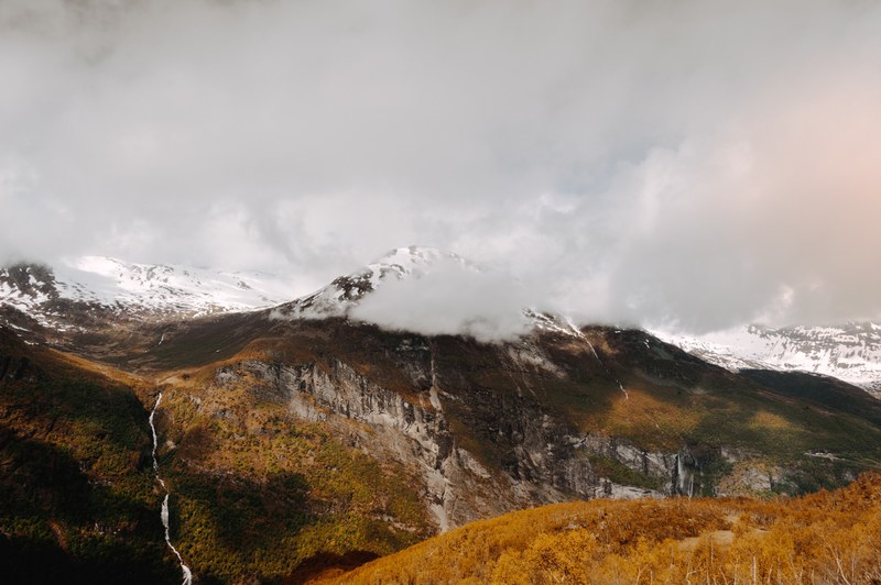 majestic view of a mountain with a stream flowing down its side and clouds enveloping its peak, norway geiranger fjord 4k