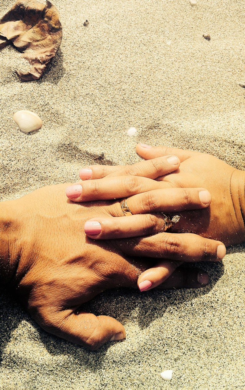 a married couple at the beach wearing wedding rings holds hands on the sand, lovers hands on sand 4k