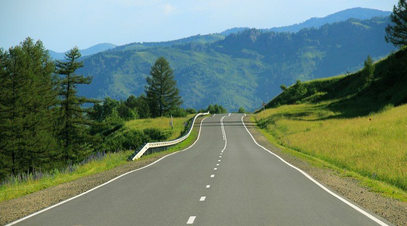an empty road around green grassy hills on a sunny day, sunny road through nature 4k