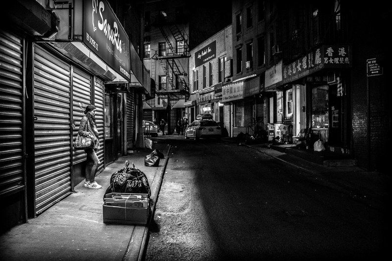black and white lone woman standing on sidewalk near closed storefront near garbage bags in chinatown, 10 bands 50 bands_ 100 bands 4k