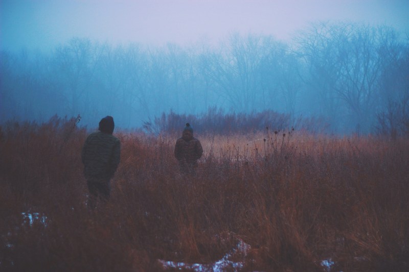 two people walking through brown grass on a cold evening, cold evening in a field 4k