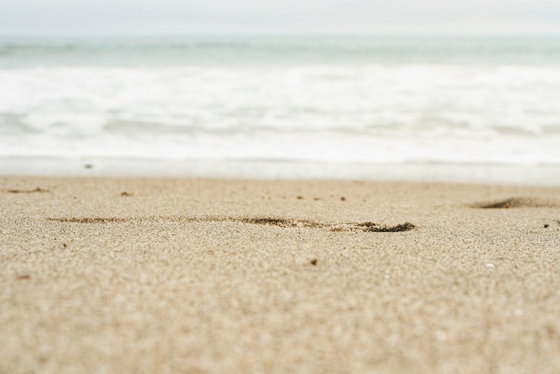beach sand focused with sea foam unfocused in the background, focused sand beach 4k