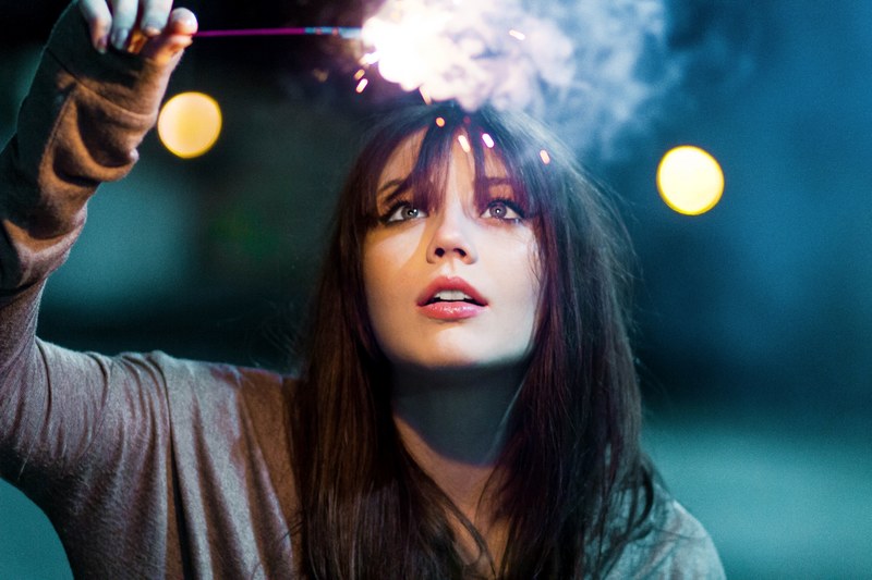 a young brunette woman holding up a sparkler at night, woman holding up a sparkler 4k