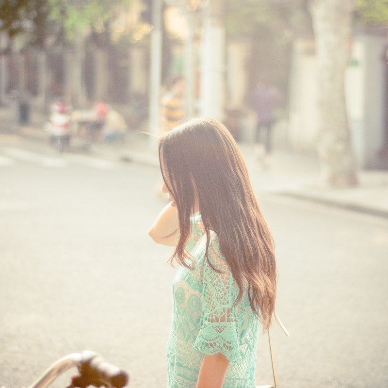 a woman in profile in a turquoise lacy top by a city street in bright sunlight, womans profile in bright sun 4k
