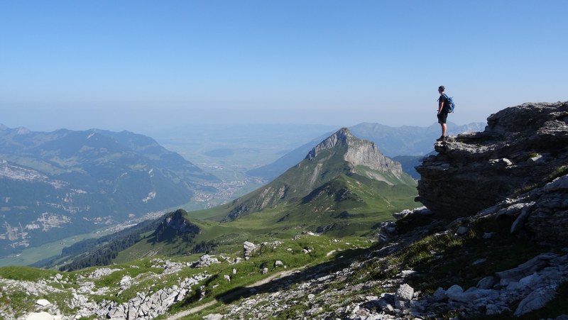 a male hiker standing on a large rock overlooking a fertile mountain valley, hiking in the mountains in schilt 4k