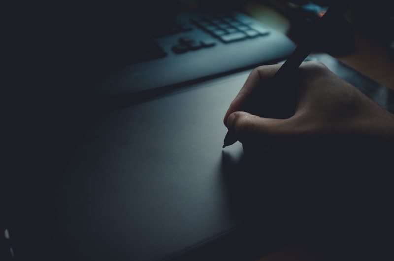 a dim shot of a person using a drawing tablet, stylus on a graphics tablet 4k