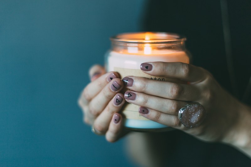 woman wearing stone ring and painted nails holds lit candle in dark light, hands 4k