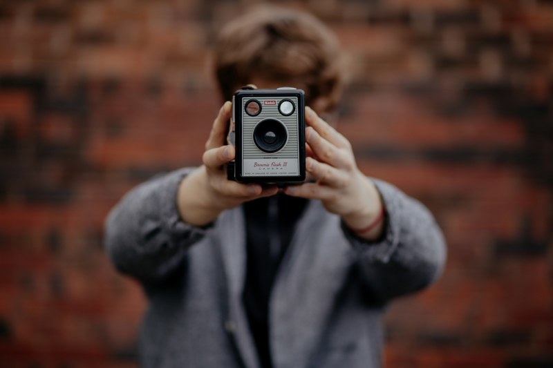 a person with short brown hair and a gray sweater taking a selfie with a vintage kodak camera covering his face, selfie with vintage camera 4k