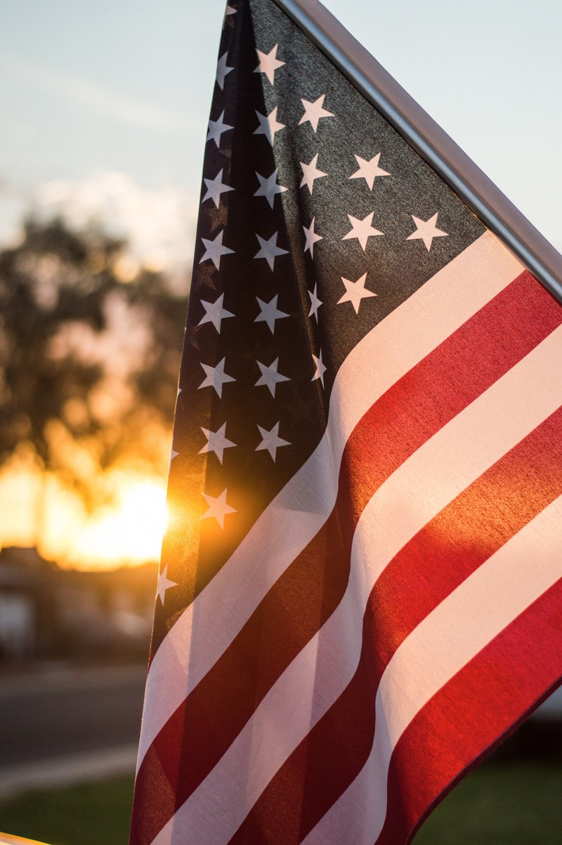 sun shines behind a patriotic american flag, usa 4k