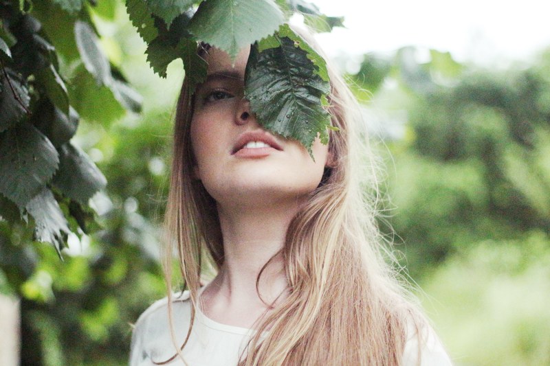 woman hiding her face behind a large leaf on a tree, hidden behind leaves 4k