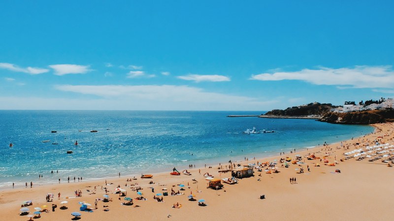 a crowded beach near a seaside town on a sunny day, tourists on a sandy shore 4k