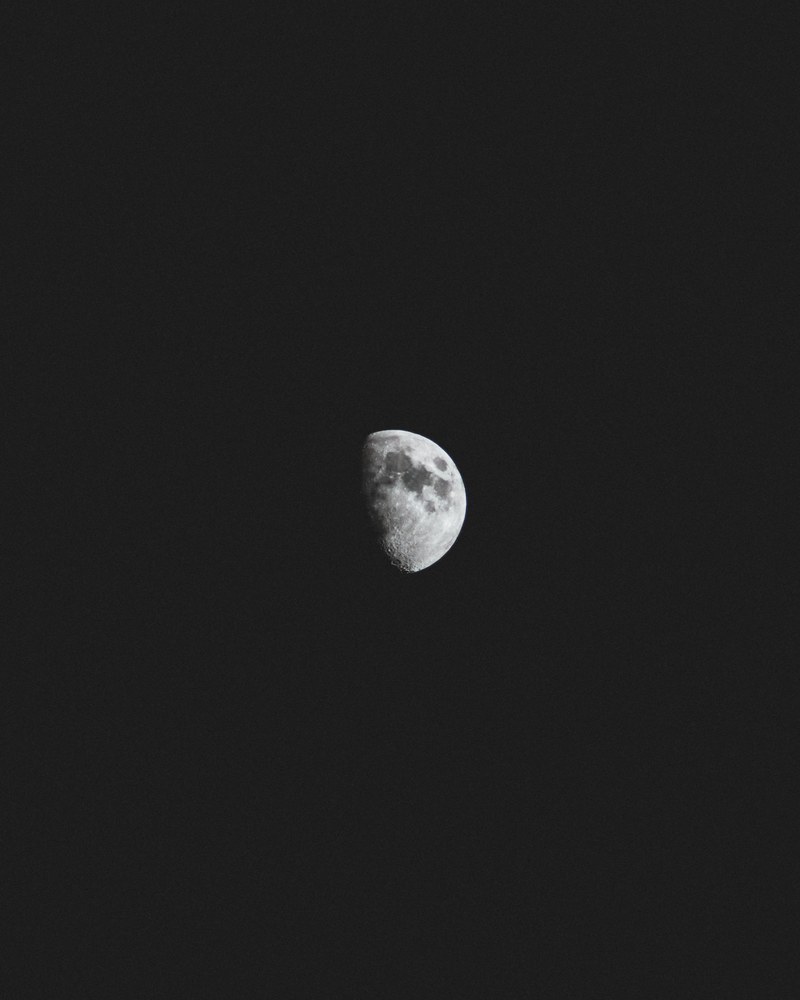 dark spots visible on a half moon against a black night sky, beyond 4k