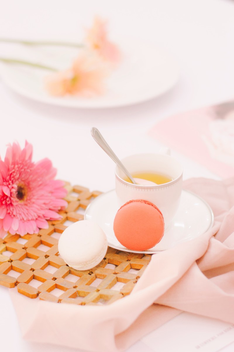 a pink gerbera flower next to a cup of tea and two macaroons, sweet tea time 4k