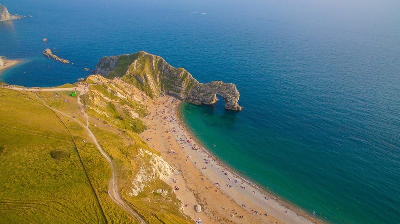 drone aerial view of a cliff with green fields on the ocean sand shoreline at durdle door, drone view of cliffs on coast 4k