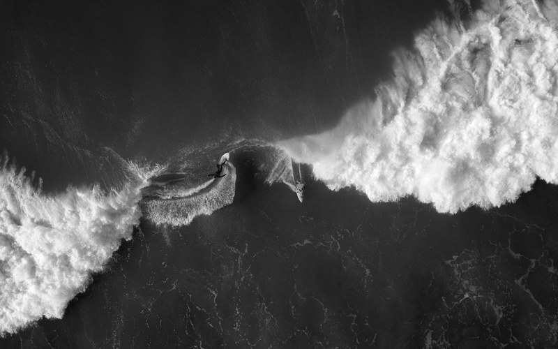 a black and white overhead drone shot of surfers riding foaming waves at gisborne new zealand, dance 4k