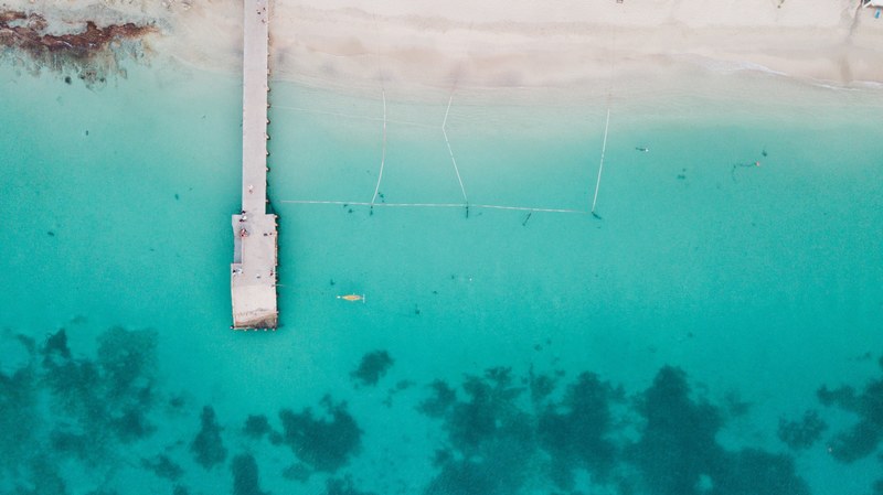 drone aerial view of the pier on the sand beach by the clear shallow ocean at grand case, drone view of a pier 4k