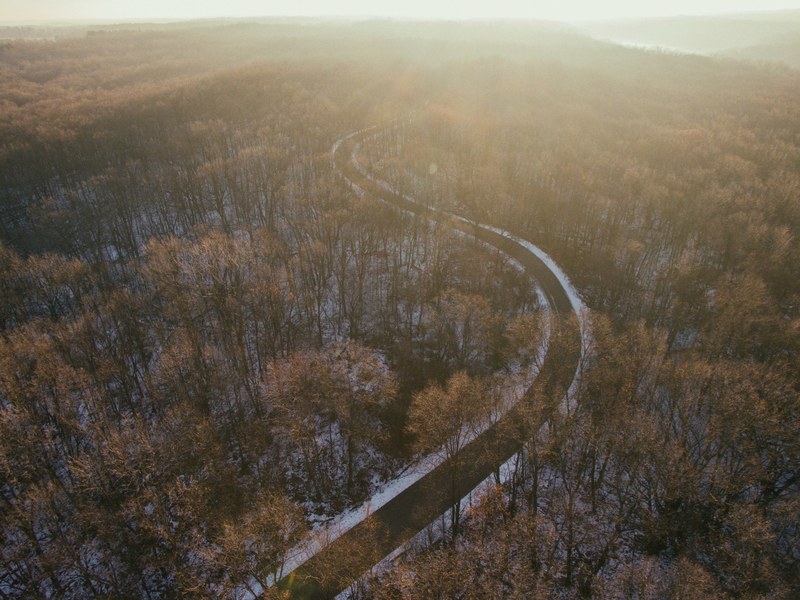 drone shot of a winding road through a forest in holly michigan on a winters day, snowy road through a forest 4k