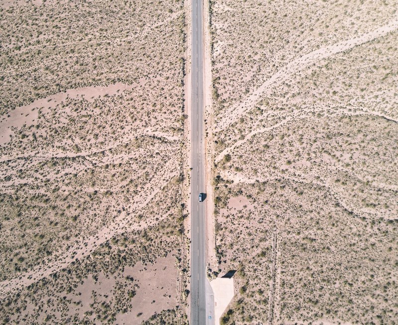 top down view of a single blue car driving down a highway cutting through a desert in nevada, _desert highway 4k