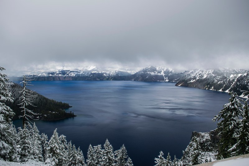 crater lake with a frozen shoreline of trees under thick gray fog and clouds, frozen crater lake 4k