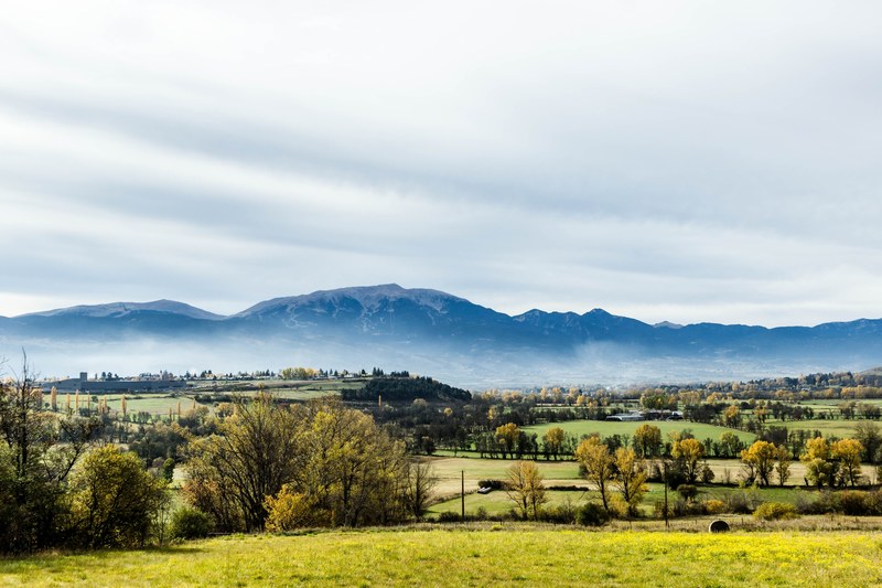 a woody countryside landscape with a snow capped mountain towering over the village, countryside under the mountain range 4k