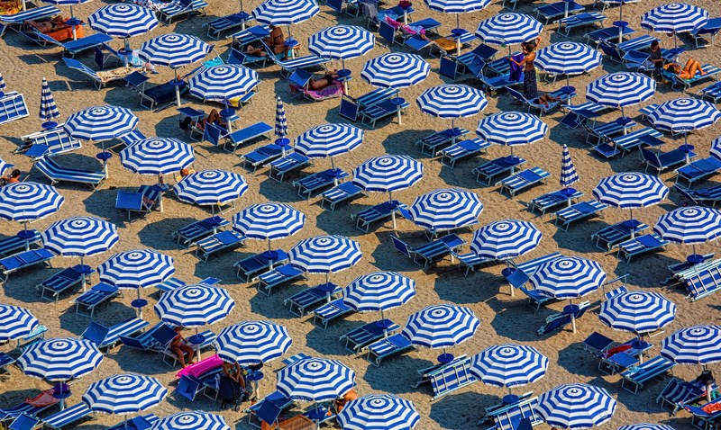 a high angle shot of rows of white and blue umbrellas over blue deck chairs lining a sandy beach, beach in white and blue 4k